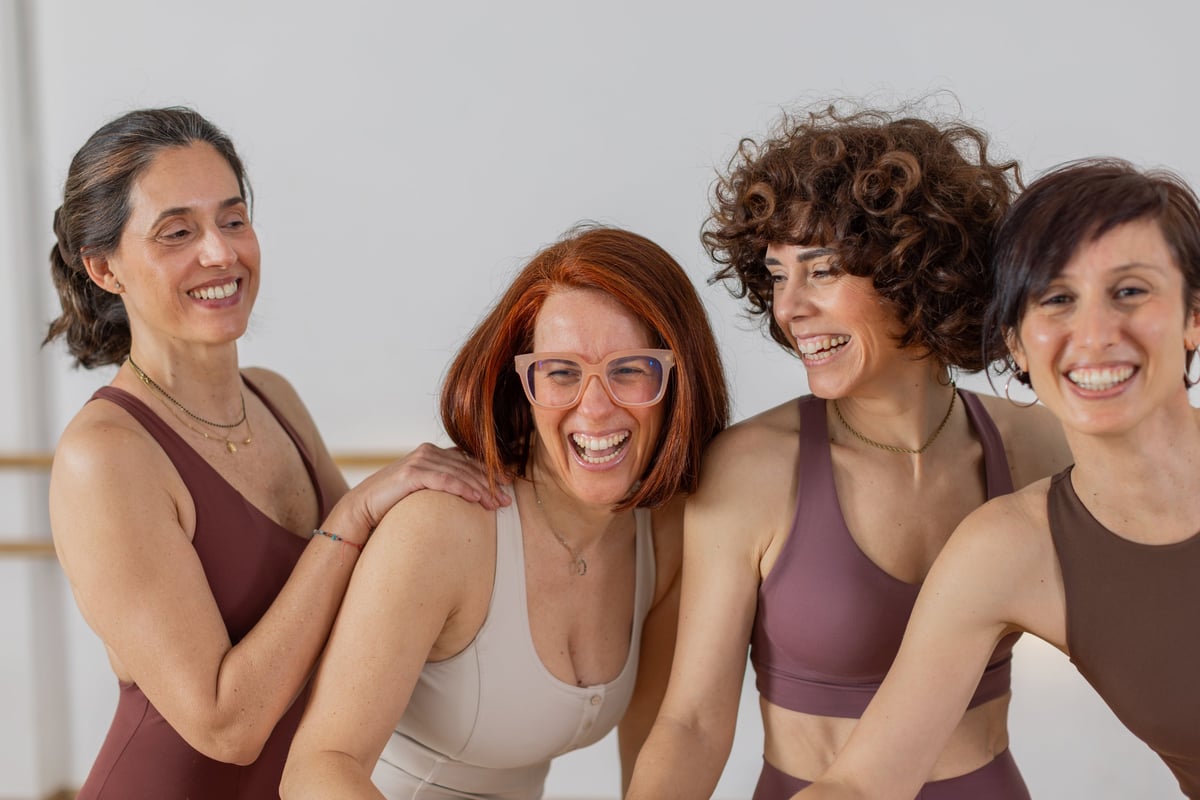 A group of women laughing together in a wellness studio, representing the friendly community feel of Wellness Reset